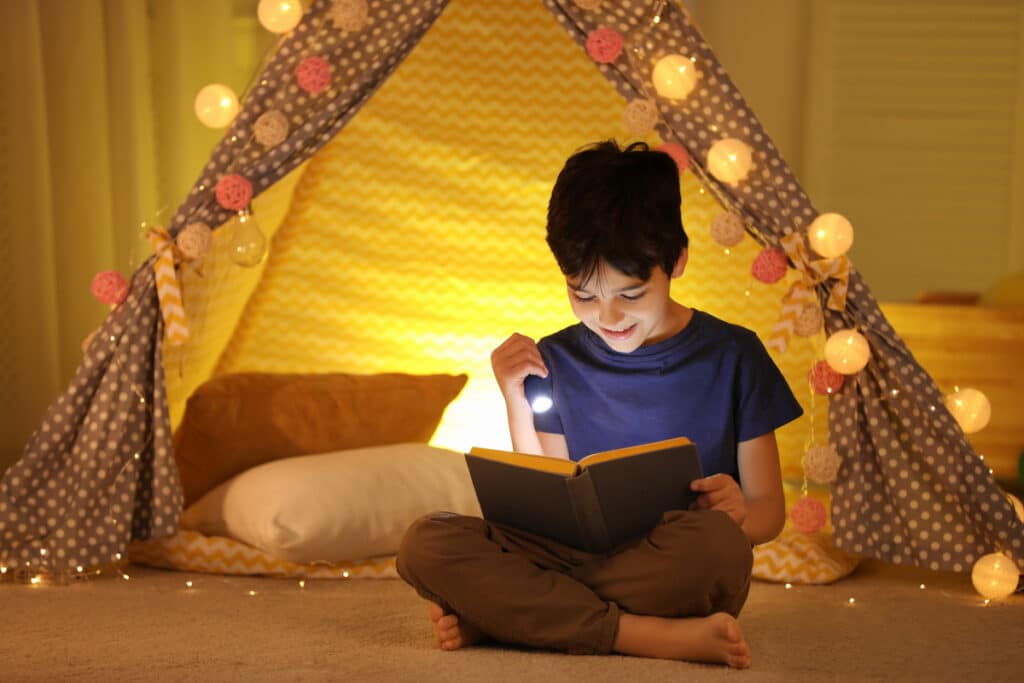 Young boy reading with flashlight